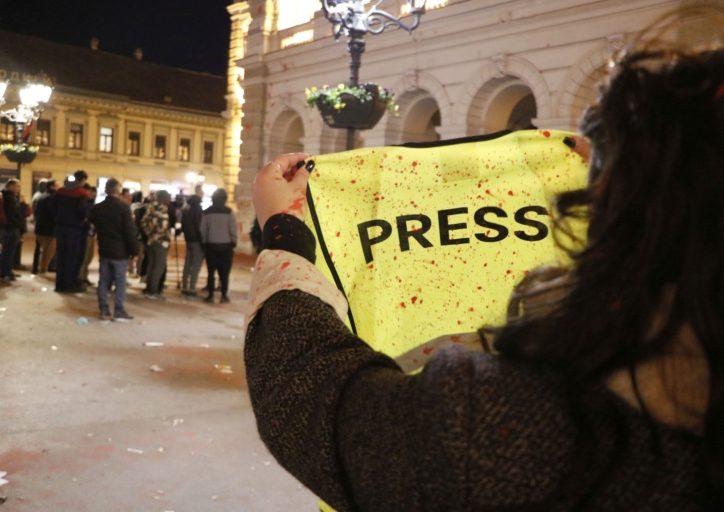 Žuti press prsluk u rukama iskapan crvenom bojom, ljudi u pozadini