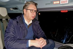 Predsenik Stbije Aleksandar Vučić sedi zamišljen u kaputu verovatno u helikopteru. Pored prozora vidi se znak Exit