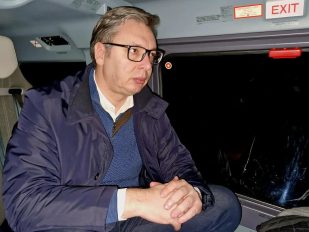 Predsenik Stbije Aleksandar Vučić sedi zamišljen u kaputu verovatno u helikopteru. Pored prozora vidi se znak Exit