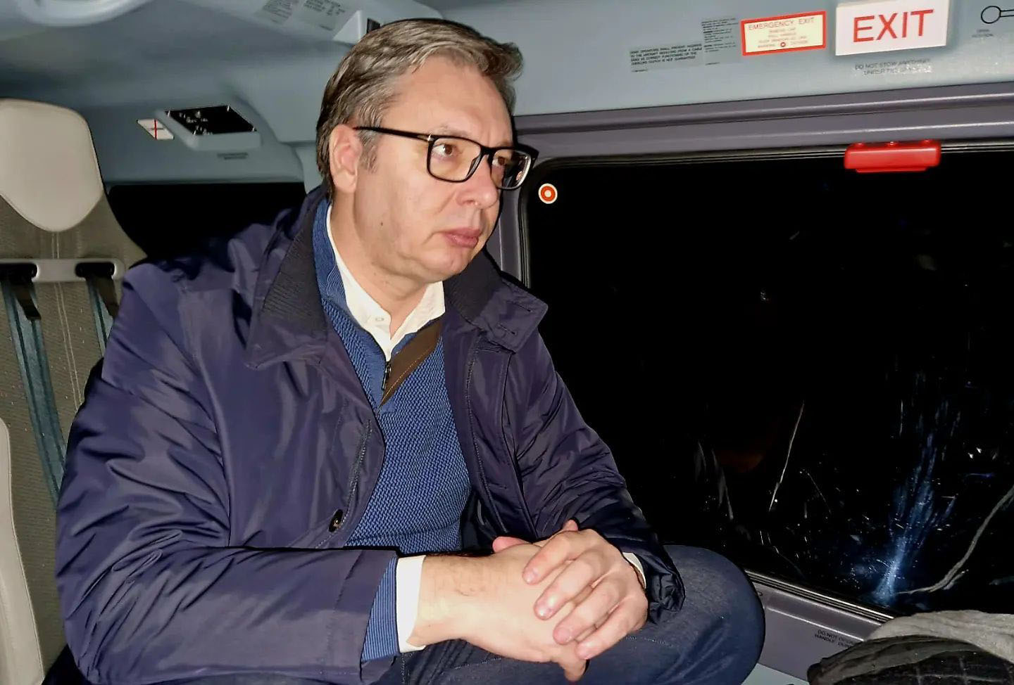 Predsenik Stbije Aleksandar Vučić sedi zamišljen u kaputu verovatno u helikopteru. Pored prozora vidi se znak Exit