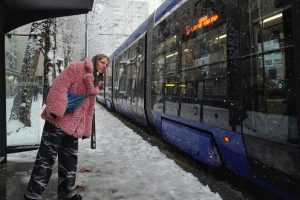 Žena gleda sa stanice tramvaja, tramvaj prolazi, sneg