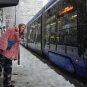 Žena gleda sa stanice tramvaja, tramvaj prolazi, sneg