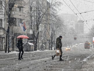 Ljudi prelaze ulicu dok pada jak sneg.