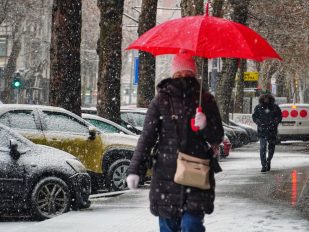 Žena sa kišobranom hoda ulicom dok pada sneg.