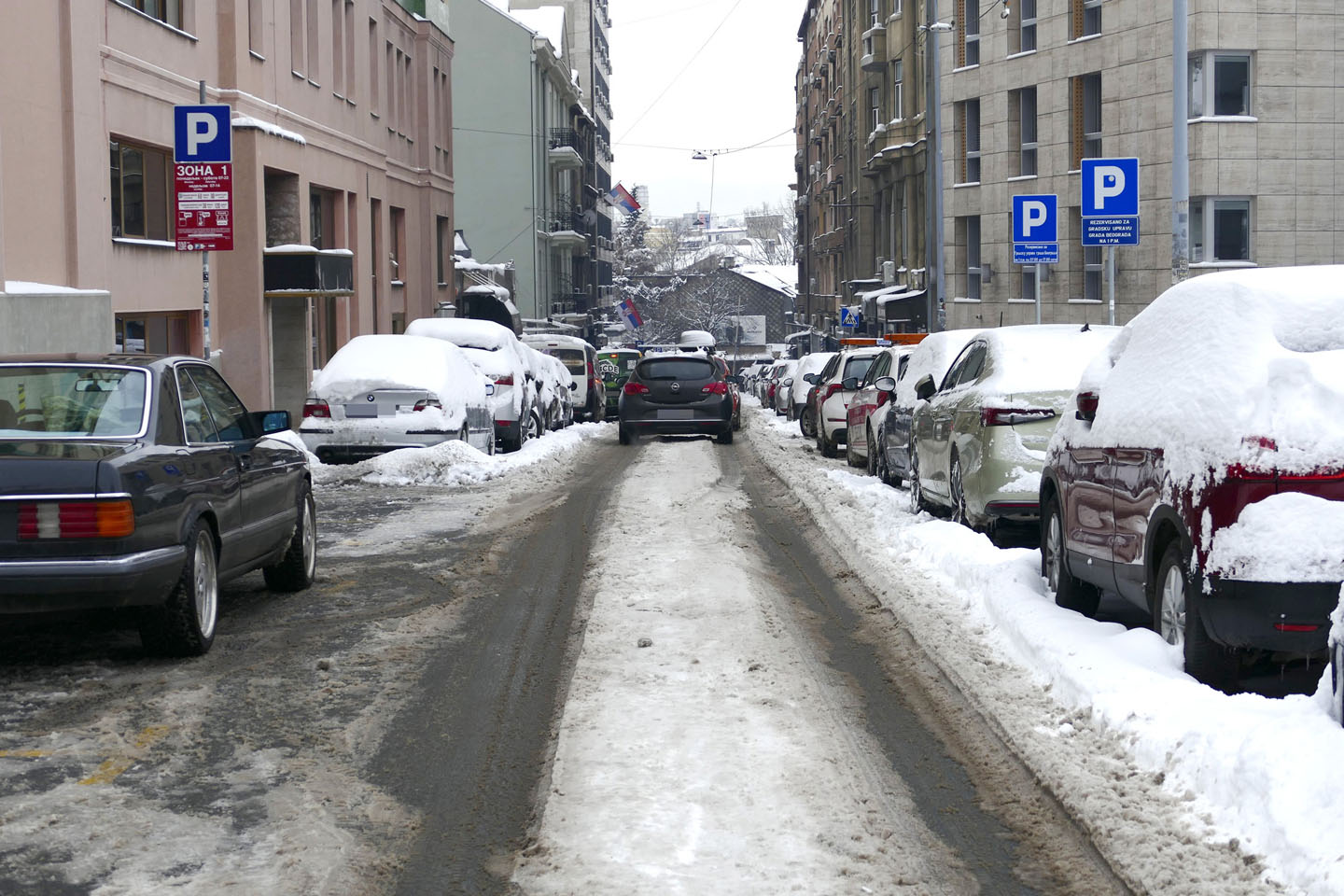 Zavejana parkirana vozila, jedno ide ulicom