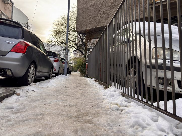 Sneg na trotoaru, parkirani automobili na parking mestima na ulici