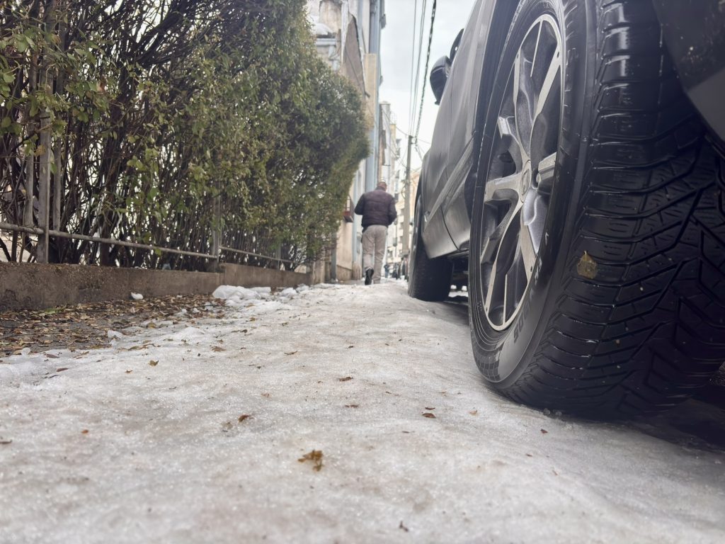 Pešak na potpuno zaleđebnom trotoaru prolazi pored parkiranih automobila