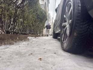 Pešak na potpuno zaleđebnom trotoaru prolazi pored parkiranih automobila