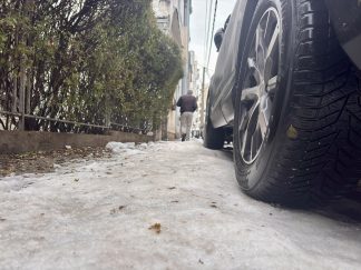 Pešak na potpuno zaleđebnom trotoaru prolazi pored parkiranih automobila