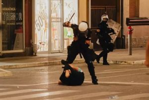 Prebijanje demonstranta u Valjevu, čovek na asfaltu, policajac sa podignutim pendrekom