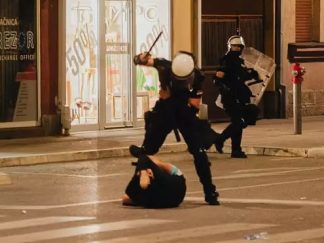 Prebijanje demonstranta u Valjevu, čovek na asfaltu, policajac sa podignutim pendrekom