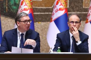Predsednik Srbije Aleksandar Vučić i premijer Đuro Macut u odelima sa kravatom. U pozadini dve zastave Srbije.