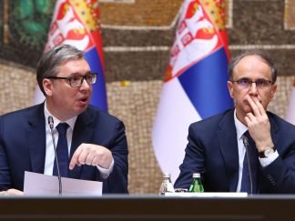 Predsednik Srbije Aleksandar Vučić i premijer Đuro Macut u odelima sa kravatom. U pozadini dve zastave Srbije.