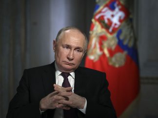 Vladimir Putin sa ukrštebnim prstima, u pozadini zastava Rusije