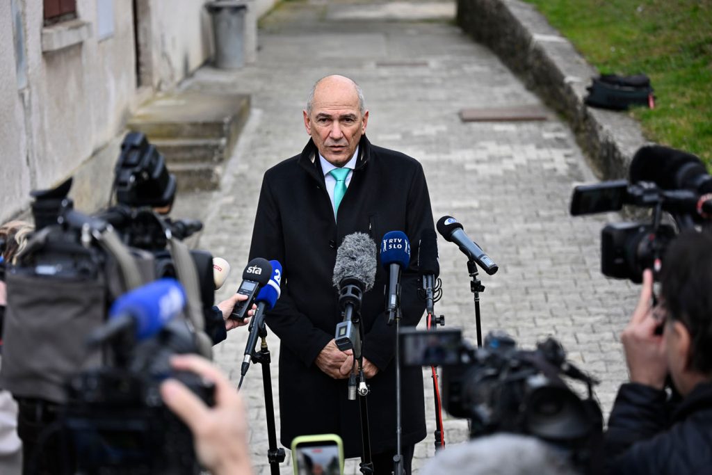 Janez Janša u kaputu sa kravatom okružen mikrofonima i kamerama