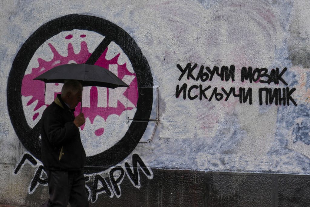 Čovek sa kišobranom prolazi pored grafita 