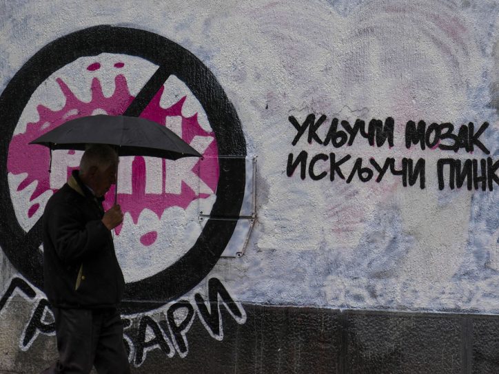 Čovek sa kišobranom prolazi pored grafita 