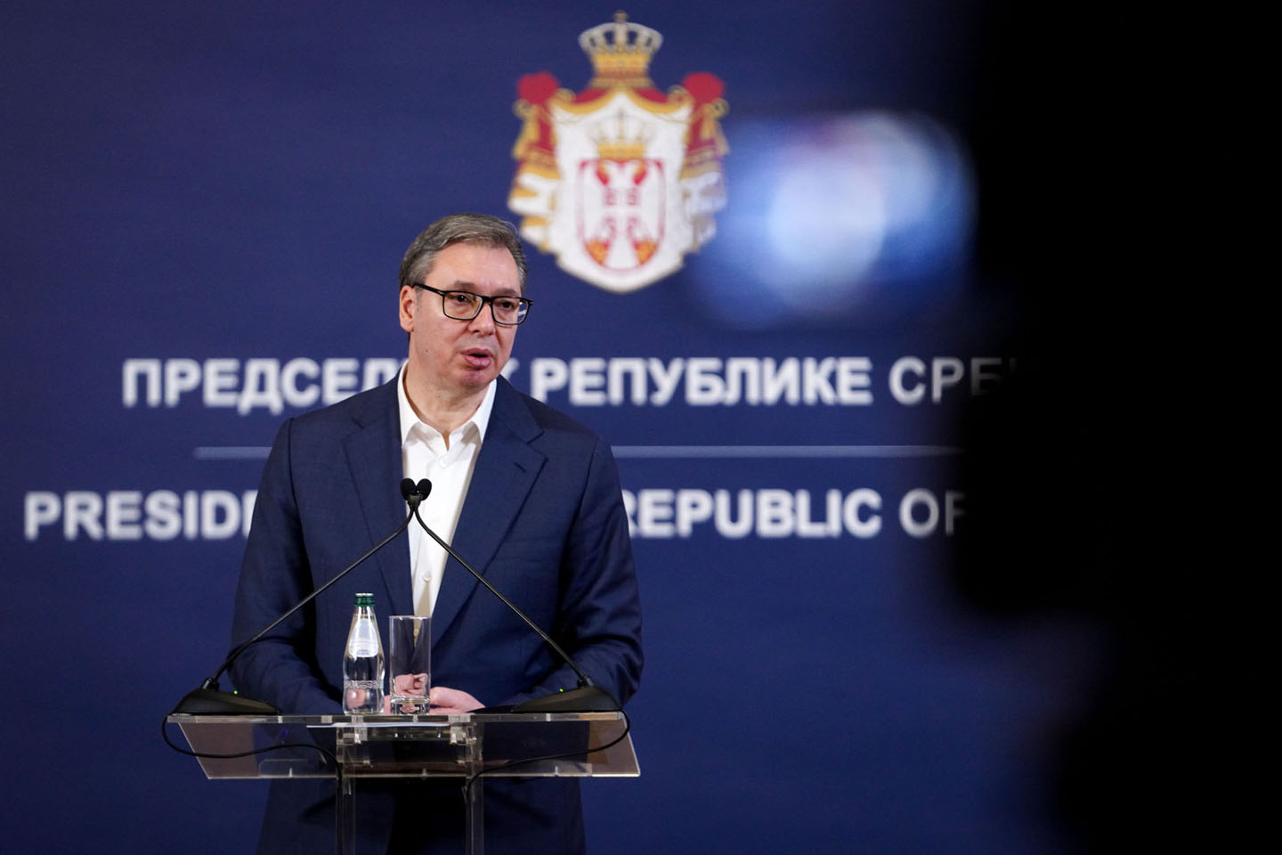 Aleksandar Vučić u teget odelu bez kravata, iza njega grb Srbije