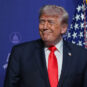 Predsednik SAD Donald Tramp se kezi sa tamni sakoom, crvenom kravatom i američkom zastavom u pozadini