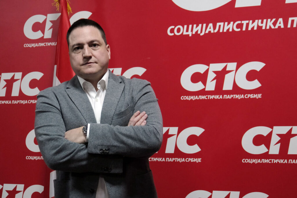 Funkcioner SPS-a Branko Ružić ispred velikog crvenog transparenta na kome piše Socijalistička partija Srbije