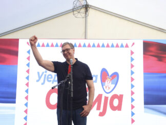 Predsednik Srbije Aleklsandar Vučić sa uzdignutom pesnicom ispred transparenta