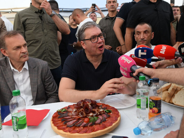Aleksandar Vučić sedi za stolom pod šatorom, pred njim meze, sokovi i mikrofovni televizija